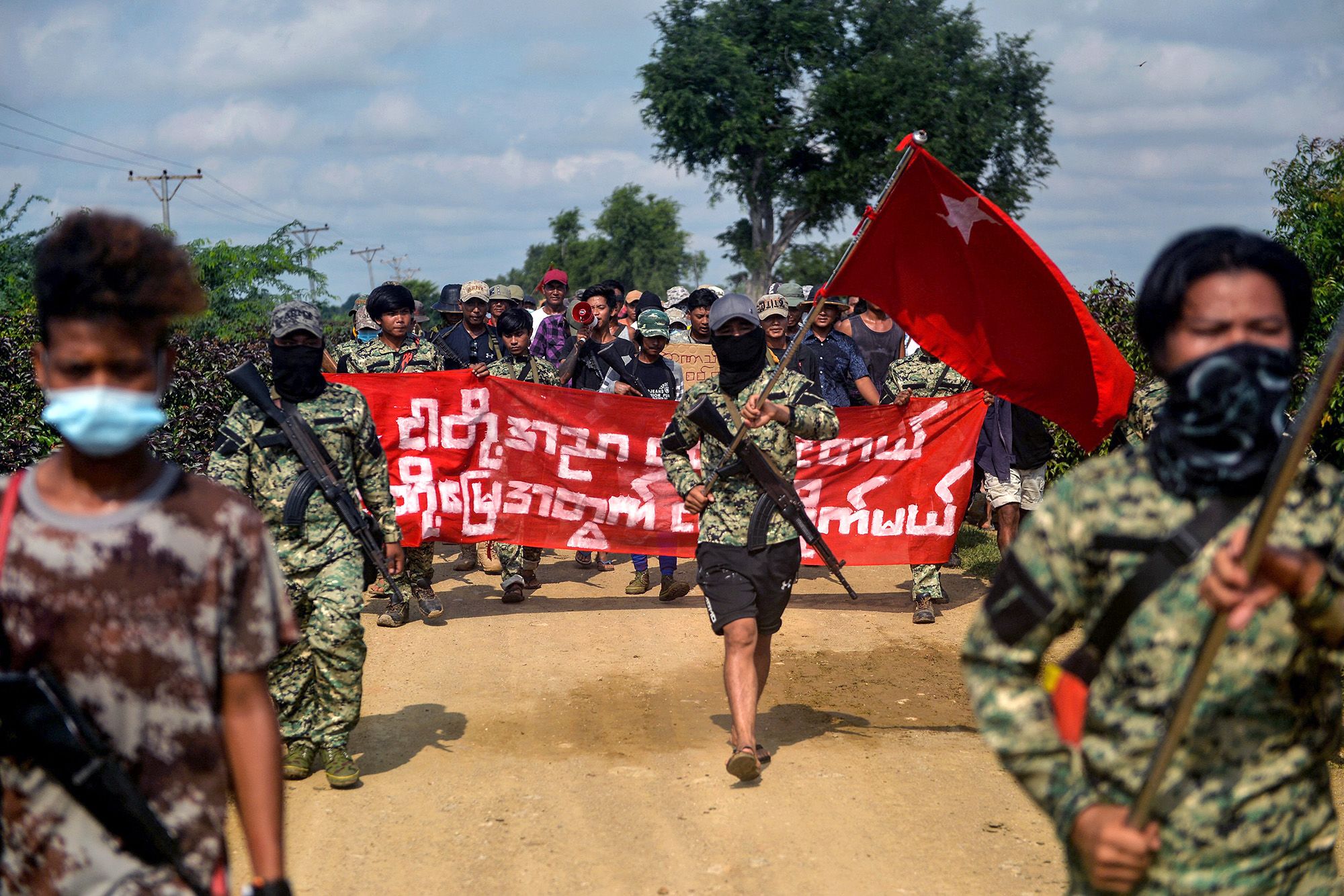 Anti-coup fighters escort protesters as they take part in a demonstration against the military coup in Sagaing, in the Sagaing Division of Myanmar on September 7, 2022. - In Myanmar's northwest Sagaing region, dozens of local Peoples Defence Forces are fighting the military and attempting to overturn the coup it carried out last year. Armed with little more than homemade weapons and knowledge of the local terrain, some of these groups have surprised the military with their effectiveness, analysts say. - TO GO WITH 'MYANMAR-CONFLICT-COUP' (Photo by AFP) / TO GO WITH 'MYANMAR-CONFLICT-COUP' (Photo by STR/AFP via Getty Images)